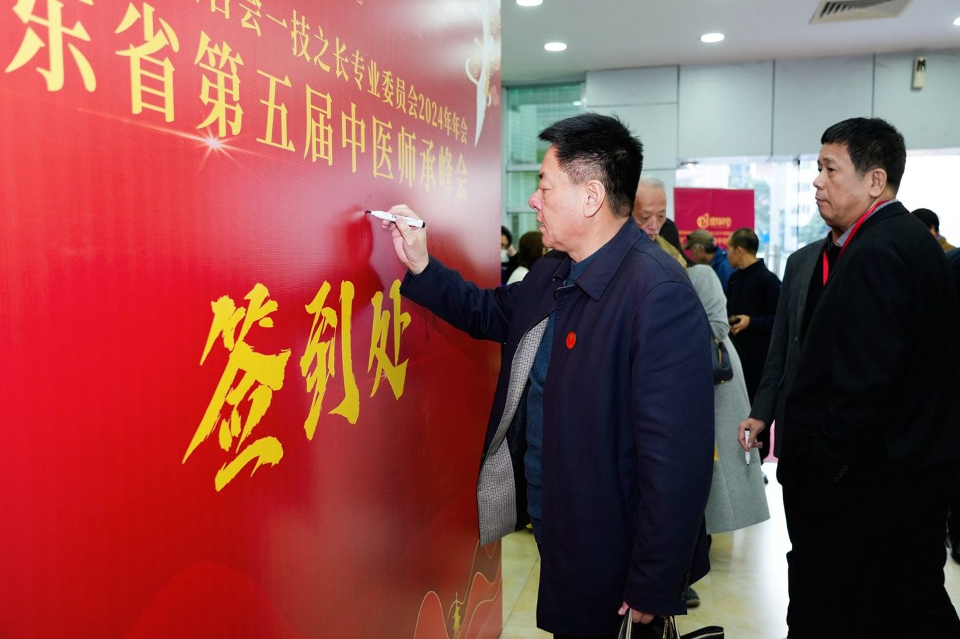 广东省第五届中医师承峰会签到处,与会嘉宾在峰会主题背景板前签到